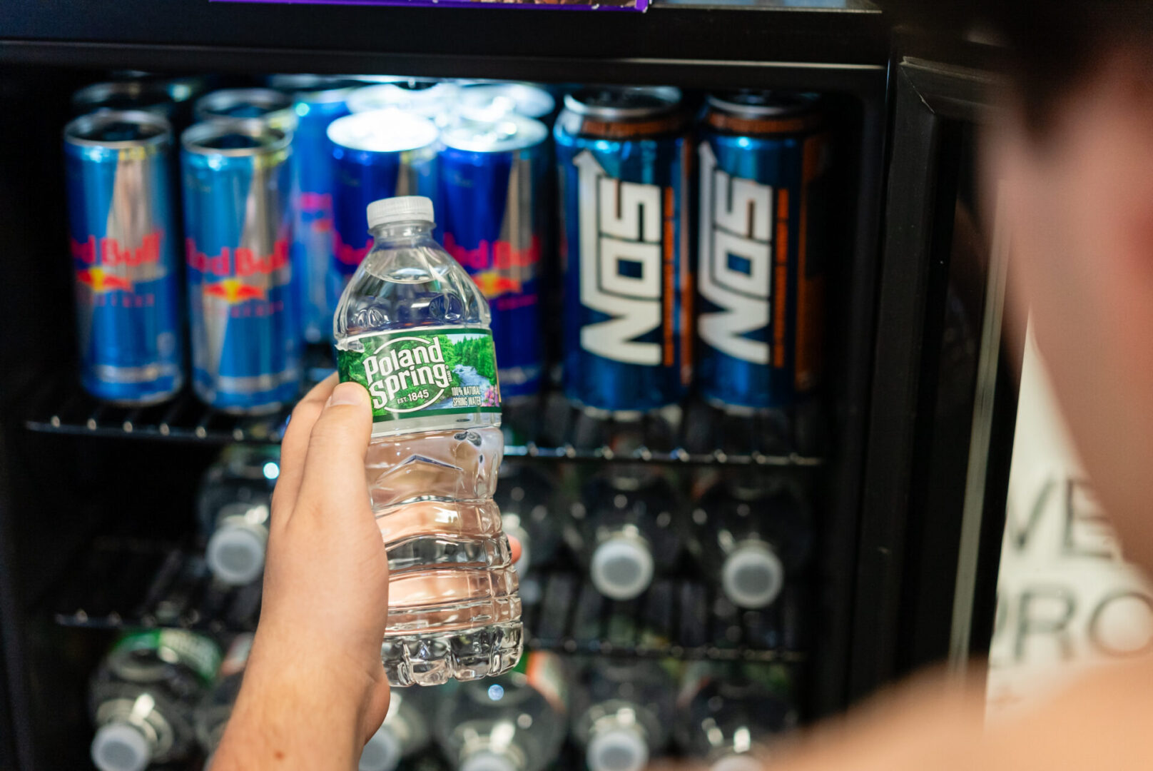 A person holding a bottle of water in front of an open refrigerator.