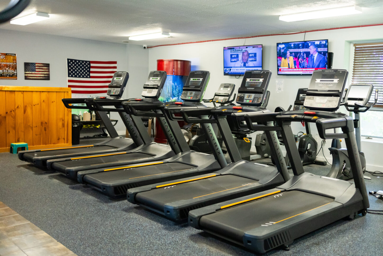 A row of treadmills in a gym with american flag on the wall.