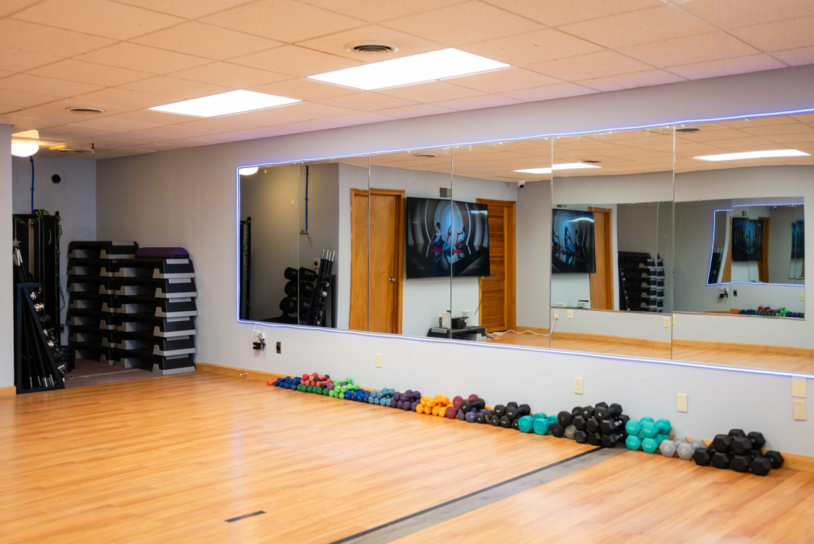 A gym with mirrors and many different colored dumbbells.